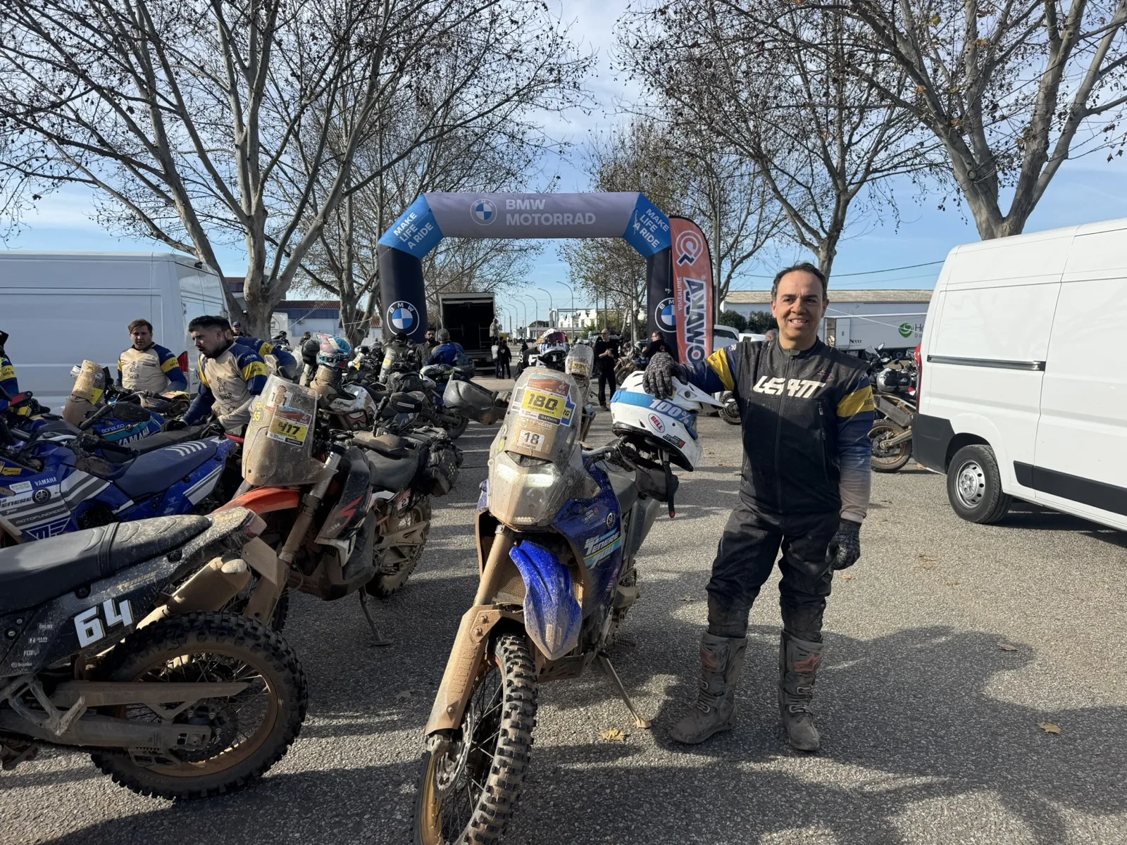 Adventure rider standing next to a mud-covered motorcycle at the end of an off-road event