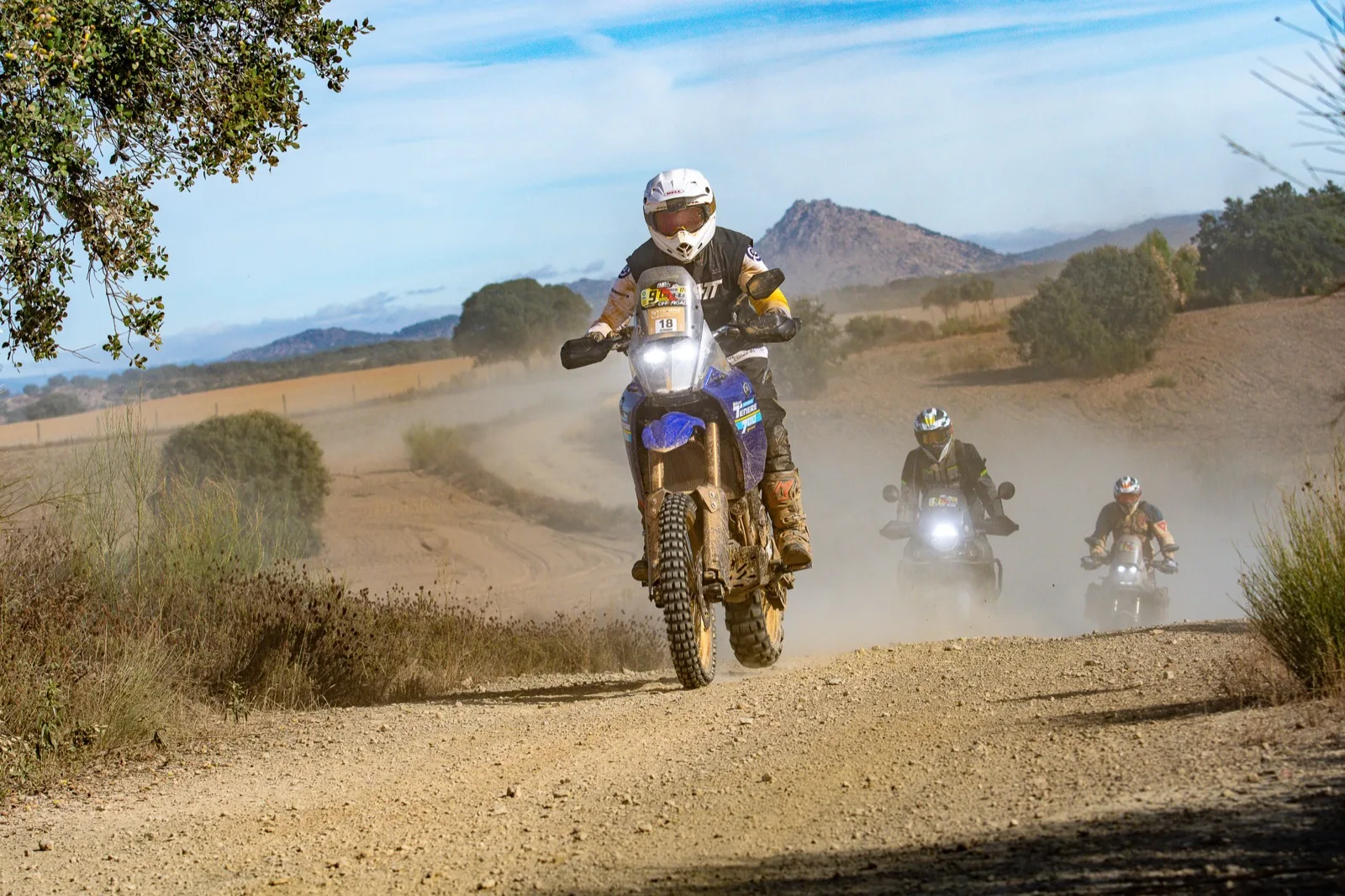 Adventure motorcycle riding a dusty gravel trail, with more riders following behind